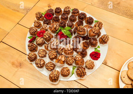 Small assorted cakes lined up decorated on dessert buffet with red rose and mint leaves on a white glass tray Stock Photo
