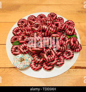 Different Vivid pink and brown donuts and one Colorful donut on a white round glass tray Stock Photo