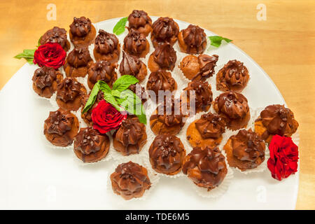 Small assorted cakes lined up decorated on dessert buffet with red rose and mint leaves on a white tray Stock Photo