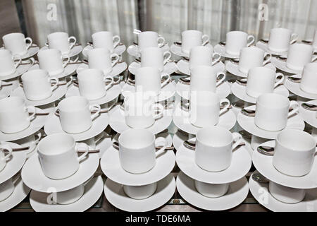 Rows of clean white coffee or tea cups, dish and spoon in a cafeteria or restaurant ready to serve a hot beverage - Empty white cups waiting for a dri Stock Photo