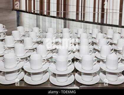 Rows of clean white coffee or tea cups, dish and spoon in a cafeteria or restaurant ready to serve a hot beverage - Empty white cups waiting for a dri Stock Photo