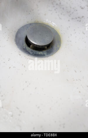 White dirty wash sink basin showing grungy drain with bits of hair. The stopper plug is a filthy nasty gross disgusting chrome stainless steel materia Stock Photo