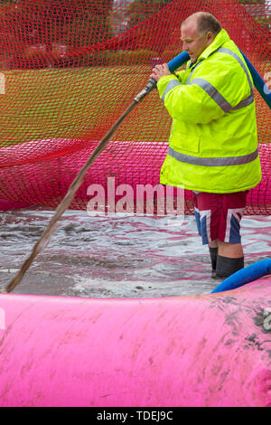 Baiter Park, Poole, Dorset, UK. 15th June 2019. Cold wet day for Race for Life Pretty Muddy. Preparing the mud pool to ensure participants get covered in mud glorious mud! Filling with hose. Credit: Carolyn Jenkins/Alamy Live News Stock Photo