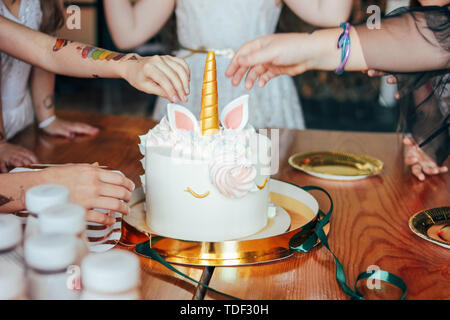 Children's hands little girls reach for the cake. Big beautiful cake unicorn on birthday of little Princess on festive table Stock Photo