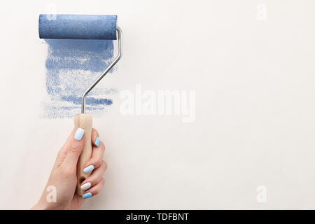 Female hand painting wall with roller in blue color, copy space Stock Photo