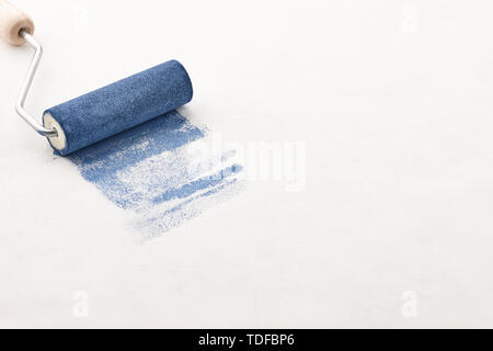 Sponge roller with blue paint on white wallpaper background, copy space Stock Photo