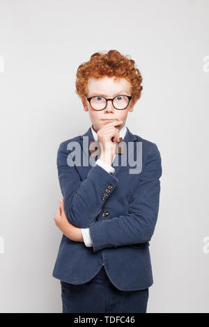 Thinking child boy with ginger hair wearing glasses and suit on white background Stock Photo