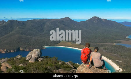 close up of two young hikers enjoying the view of wineglass bay from mt amos in freycinet national park the east coast of tasmania, australia Stock Photo