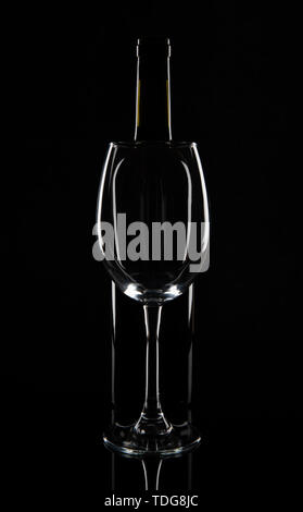 Empty wine glass in front of the wine bottle, isolated on black background. Stock Photo