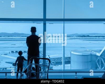 Silhouettes of father and son together at the airport, in the departure terminal, are looking through pan-window at airfield with planes. Abstract Stock Photo