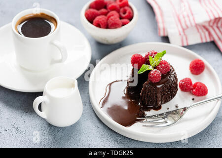 Hot Chocolate lava cake or chocolate fondant on white plate with raspberries and cup of coffee Stock Photo