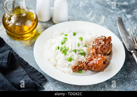 Teriyaki chicken thighs with white rice and green peas on a plate. Healthy tasty dinner Stock Photo