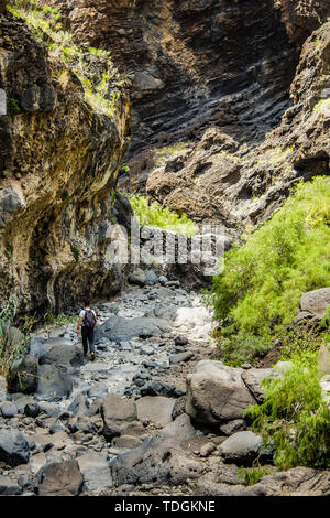 Rocks in the Masca gorge, Tenerife, showing solidified volcanic lava flow layers and arch formation. The ravine or barranco leads down to the ocean fr Stock Photo