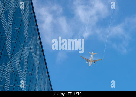 Airplan leaves a trail in the blue sky. Airliner is takking off over the building. White cloud in the blue sky in which the plane flies Stock Photo