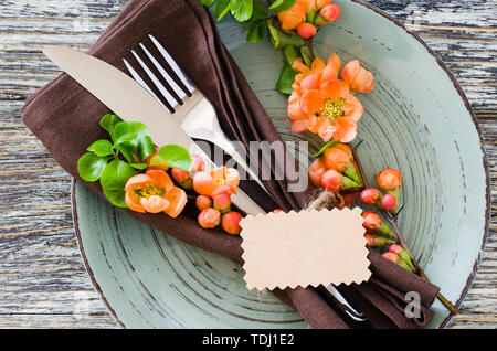 Vintage table setting with delicate flowers and tag on a linen napkin on on rustic shabby table, close-up. Holiday Table Set with floral decor Stock Photo