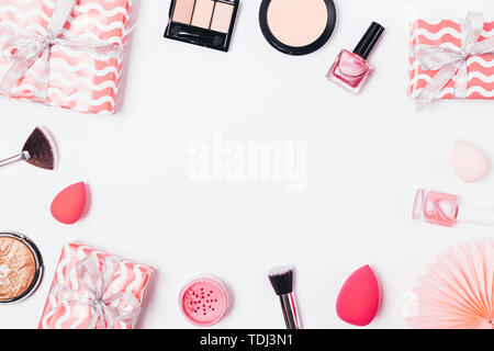 Festive flat lay frame of makeup products and pink gift boxes on white background, overhead view. Stock Photo