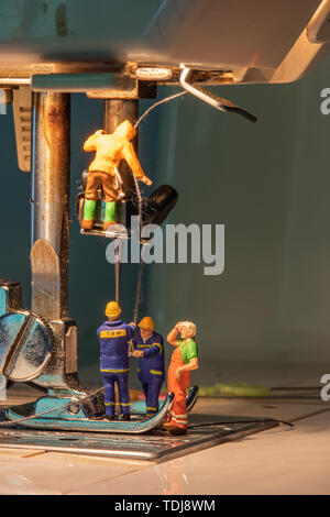Miniature people change thread on sewing machine. Stock Photo