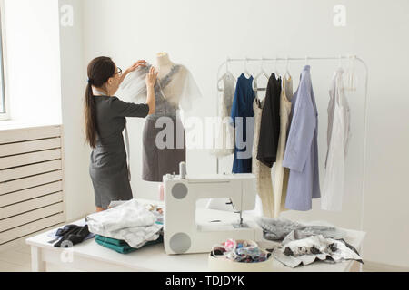Dressmaker, fashion designer, tailor and people concept - designer dressed in stylish outfit measuring materials on mannequin Stock Photo