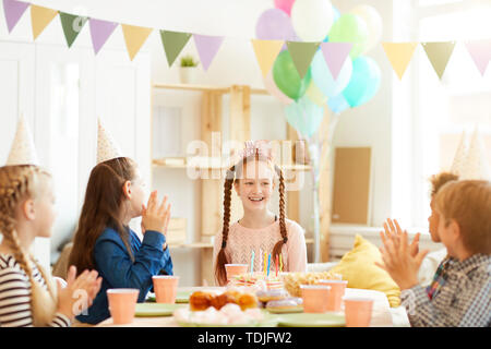 Group of children celebrating birthday at party table with happy red haired girl in center, copy space Stock Photo