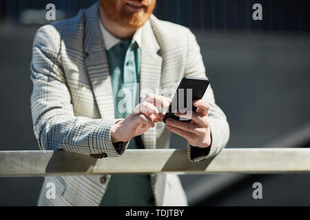 Close-up of busy bearded businessman in checkered jacket leaning on railing and using gadget outdoor Stock Photo