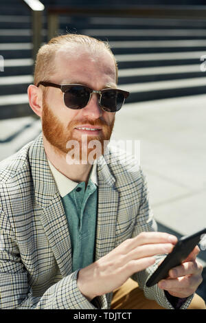 Portrait of smiling confident hipster man with red beard wearing checkered jacket using phone for work Stock Photo