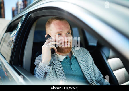 Content pensive young businessman in fashionable outfit sitting inside of car with open window and talking on phone Stock Photo