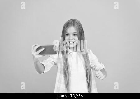 Video call concept. Girl hold smartphone taking selfie. Selfie for social networks. Streaming online or shooting vlog. Hello world this is my channel. Let me take selfie. Child girl hold smartphone. Stock Photo