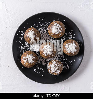 Healthy organic energy balls made with dates, prunes, raisins, peanut, with coconut shavings, in black plate on white background, flat lay. Stock Photo