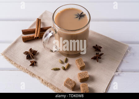 Indian traditional Masala chai tea in a glass mug and kitchen herbs, over white table background with copy space for text. Stock Photo