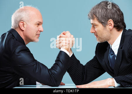 Two businessmen facing off against each other in a challenge for supremacy arm wrestling over an office table with looks of determination in a close u Stock Photo