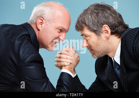 Two determined businessmen going head to head in a challenge for supremacy staring into each others eyes and arm wrestling Stock Photo