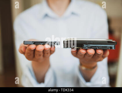 IT woman holding presenting two different generations of computer disks HDD hard disk drive and SSD solid state drive - offering them to viewer Stock Photo