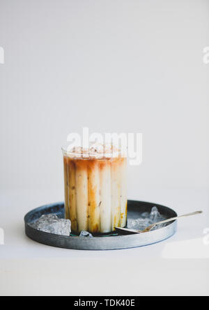 Summer cold refreshing drink coffee cocktail. Ice caramel macchiato coffee with caramel vanilla syrup in glass on metal serving plate, white backgroun Stock Photo