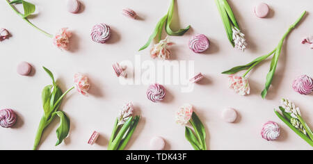 Flat-lay of sweet pink macaron cookies, lilac marshmallows and fresh spring flowers over pastel pink background, top view. Food texture, background an Stock Photo