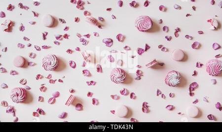 Flat-lay of sweet pink macaron cookies, lilac marshmallows and rose petals over pastel pink background, top view. Food texture, background and wallpap Stock Photo