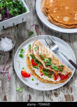 Crepes filled ricotta and vegetables with microgreens served on white plate Stock Photo