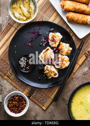 Asian dinner set. Pork dumplings served on the black plate. Egg rolls on the side. Stock Photo