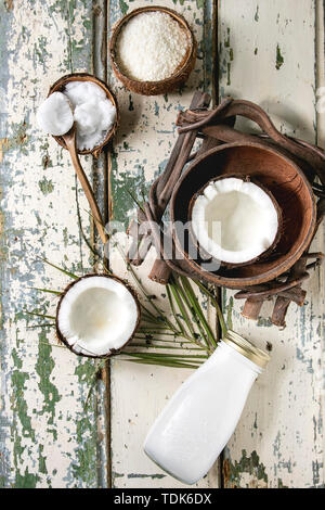 Variety of coconut products milk in glass bottle, oil and flakes in shell, fresh broken coconut on old wooden plank background. Healthy eating. Flat l Stock Photo