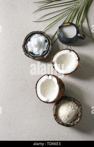 Variety of coconut products milk in jug, oil and flakes in ceramic bowls, fresh broken coconut on grey spotted background. Healthy eating. Flat lay, s Stock Photo