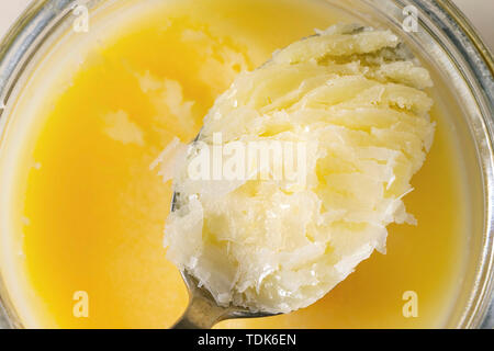 Homemade melted ghee clarified butter in open glass jar and spoon. Close up macro food background Stock Photo