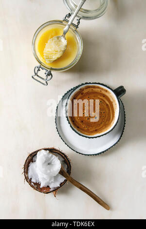 Bulletproof coffee. Keto diet coffee in blue ceramic cup with organic ghee butter and coconut cold press oil in spoons over white marble background. F Stock Photo