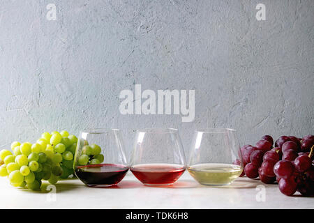 Variety of wine. Red, rose and white wine in old fashion glasses with bunches of grapes on white marble table. Copy space Stock Photo