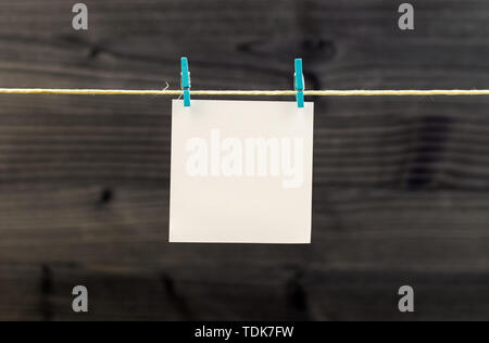 Empty white paper hanging on rope with clothespins against wooden backdrop, copy space Stock Photo