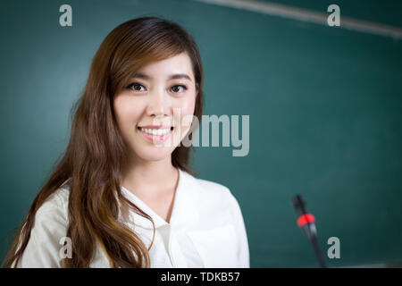 Asian beautiful woman speaking in front of blackboard with micro Stock Photo