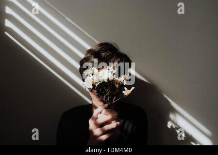 Male holding a small bouquet of flowers in front of his face with light lines shining on him Stock Photo