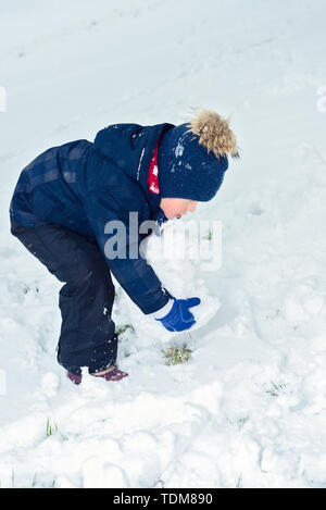 little boy makes a snowman in winter. child rolls a snowball. happy kid plays and smiles. Emotion and happiness on children's holidays Stock Photo
