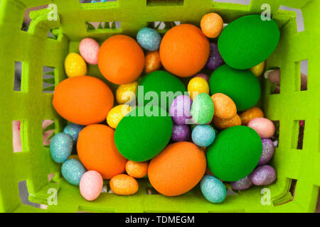 Eggs of birds of different colors and sizes lie in a green basket. Artificial products imitating poultry eggs. Easter colorful eggs of different sizes in a basket Stock Photo