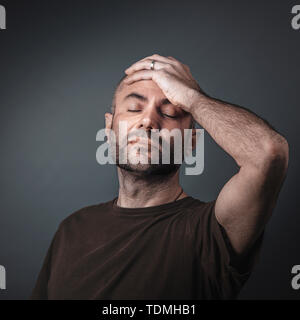 portrait of caucasian man with beard and short shackles, hand on forehead and eyes closed. Studio shot. Stock Photo