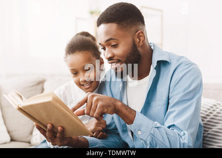 African Dad And Daughter Reading Book Together At Home Stock Photo