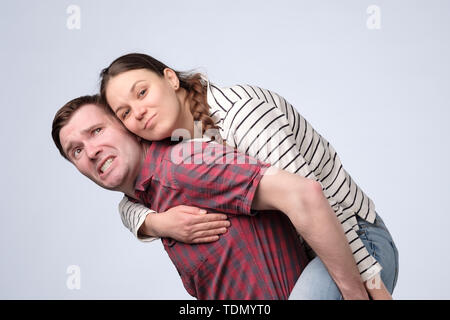 Smiling couple embracing in piggy back and looking at camera on white background Stock Photo